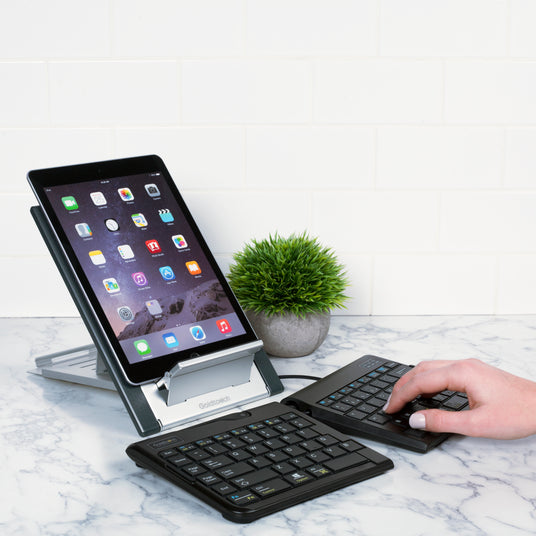 Woman typing on a Goldtouch Go!2 Mobile Keyboard paired to an iPad, brought up to eye level using a Goldtouch Go! Travel Laptop and Tablet Stand.